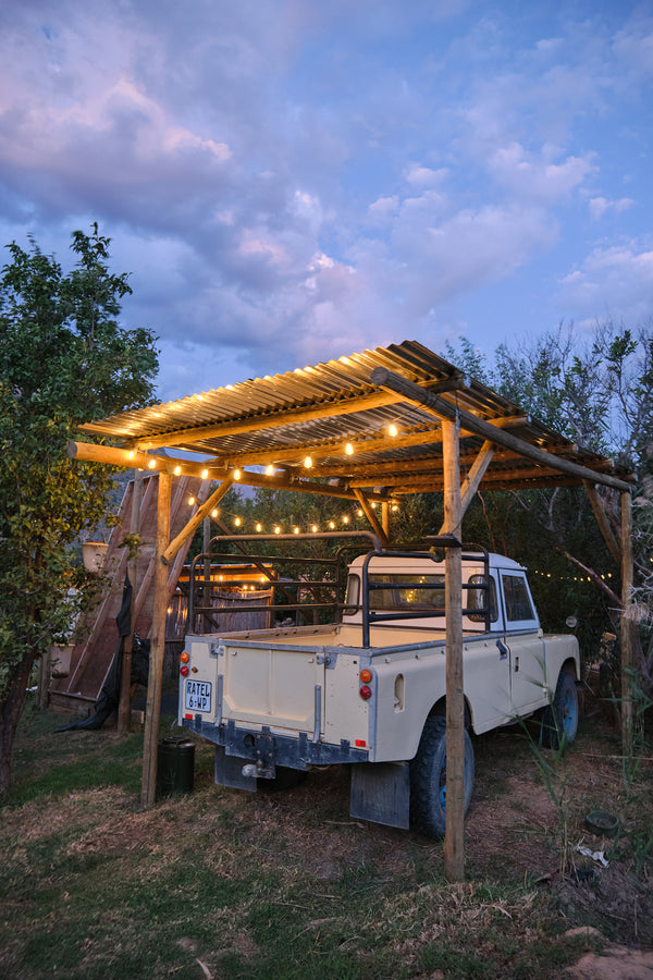 Wooden pergola with string lights over a vintage truck in a natural setting