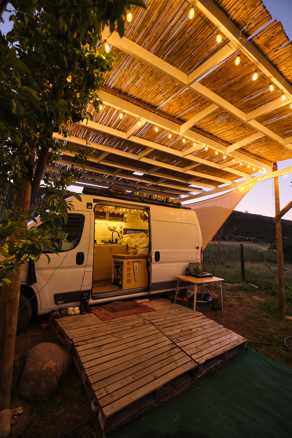Van conversion with wooden deck and thatched roof with string lights at night