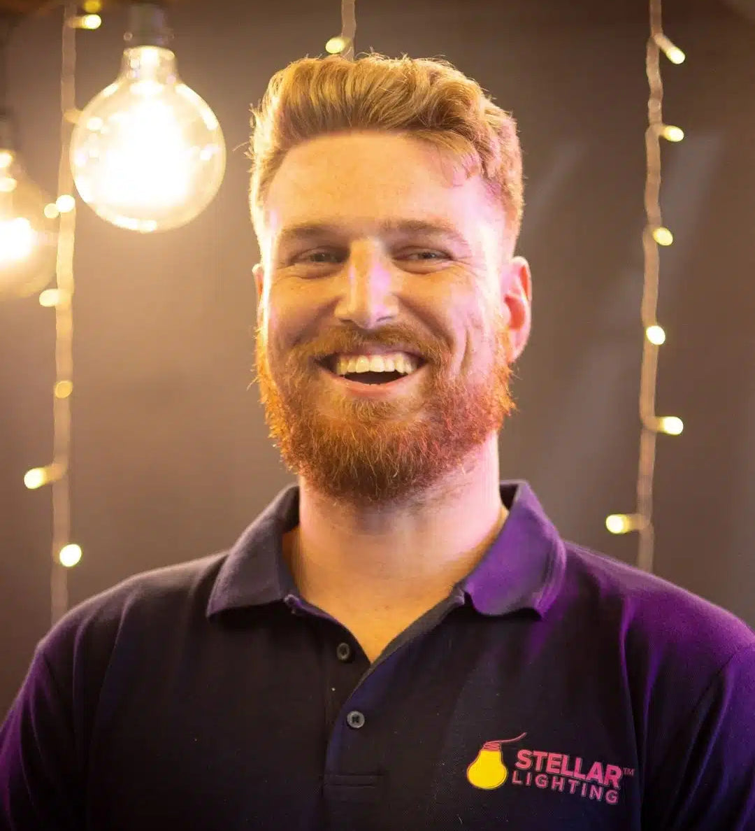 Man wearing a blue shirt with a Stellar Lighting logo, standing in front of string lights.