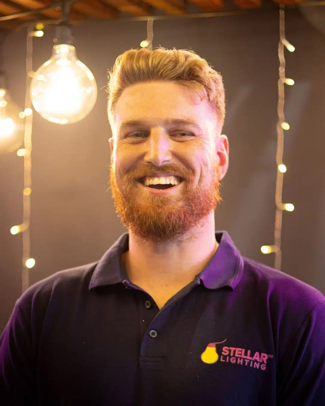 Man wearing a blue shirt with a Stellar Lighting logo, standing in front of string lights.