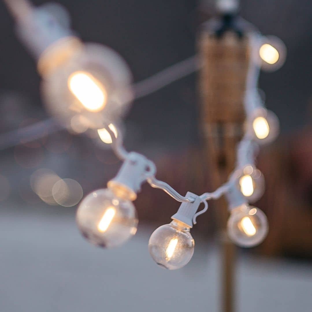 Plug-in 5m 16 LED Bulbs String Light illuminating a garden with a warm white glow, draped around trees and along a patio.