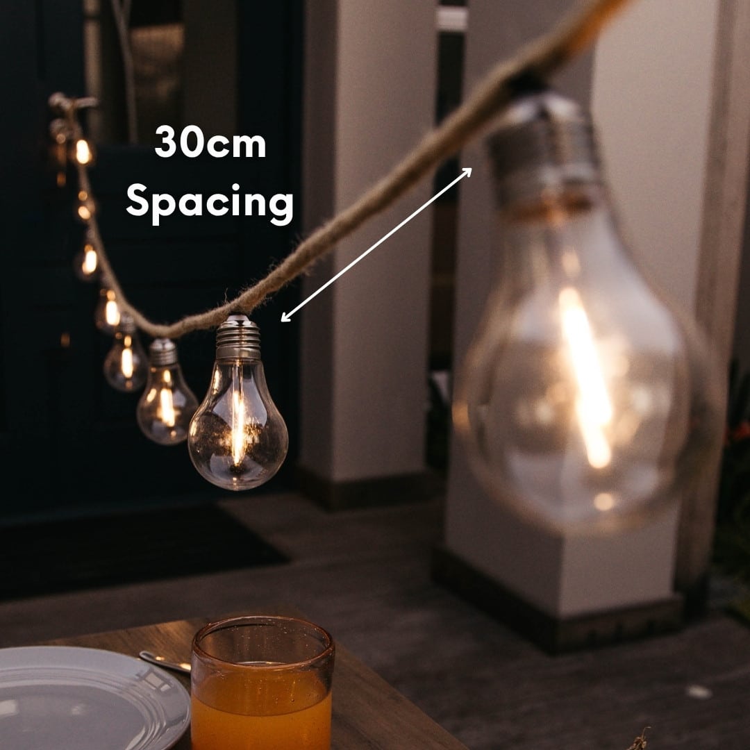 Solar powered cotton string lights with 10 warm LED bulbs hanging in a cosy covered patio setting.