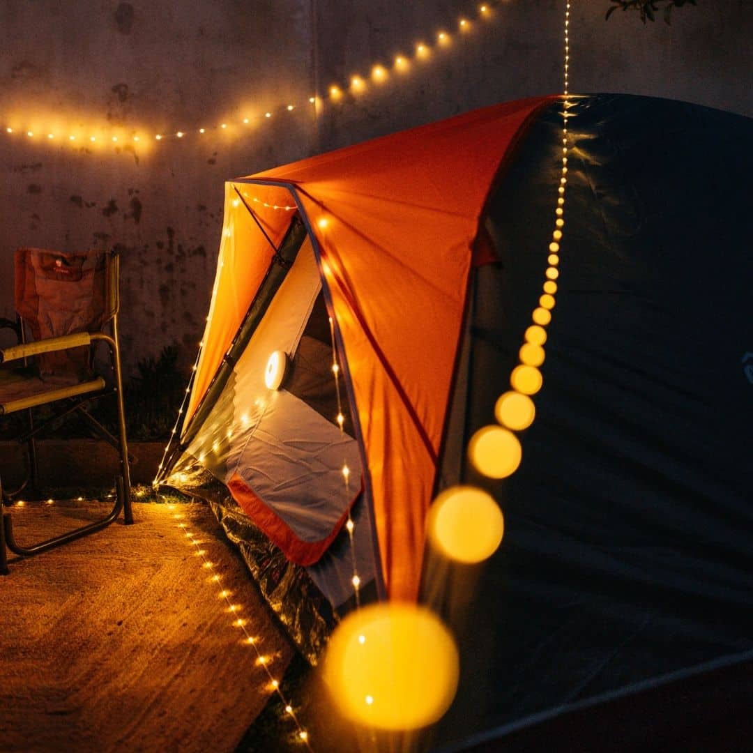 LED camping string light and rechargeable speaker lantern glowing in a cozy outdoor setting.