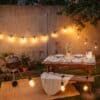 Outdoor string lights and speaker lantern illuminating a braai area at dusk.