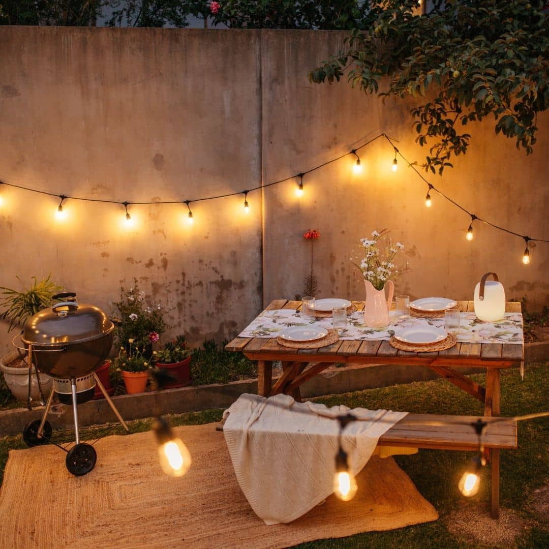 Outdoor string lights and speaker lantern illuminating a braai area at dusk.