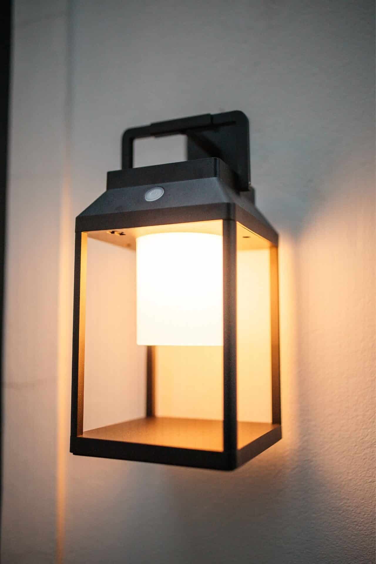 Black solar LED lantern mounted on outdoor wall with soft glow