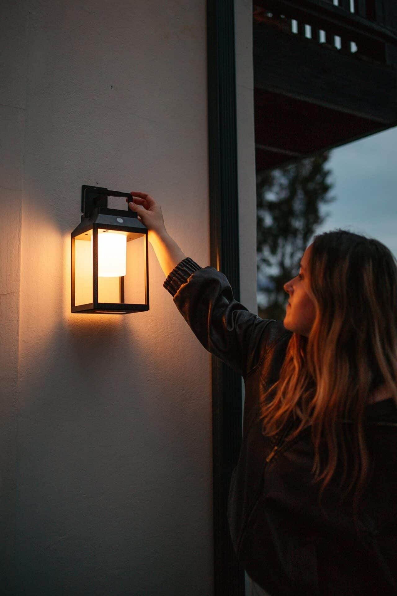 Black solar LED lantern mounted on outdoor wall with soft glow