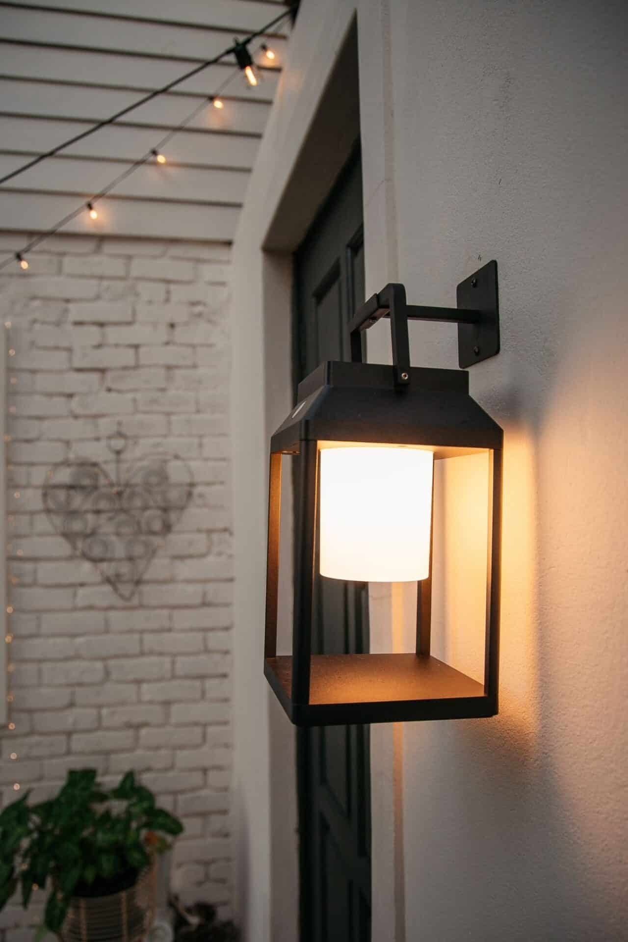 Black solar LED lantern mounted on outdoor wall with soft glow