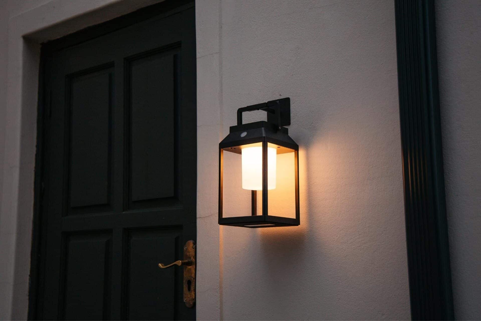 Black solar LED lantern mounted on outdoor wall with soft glow