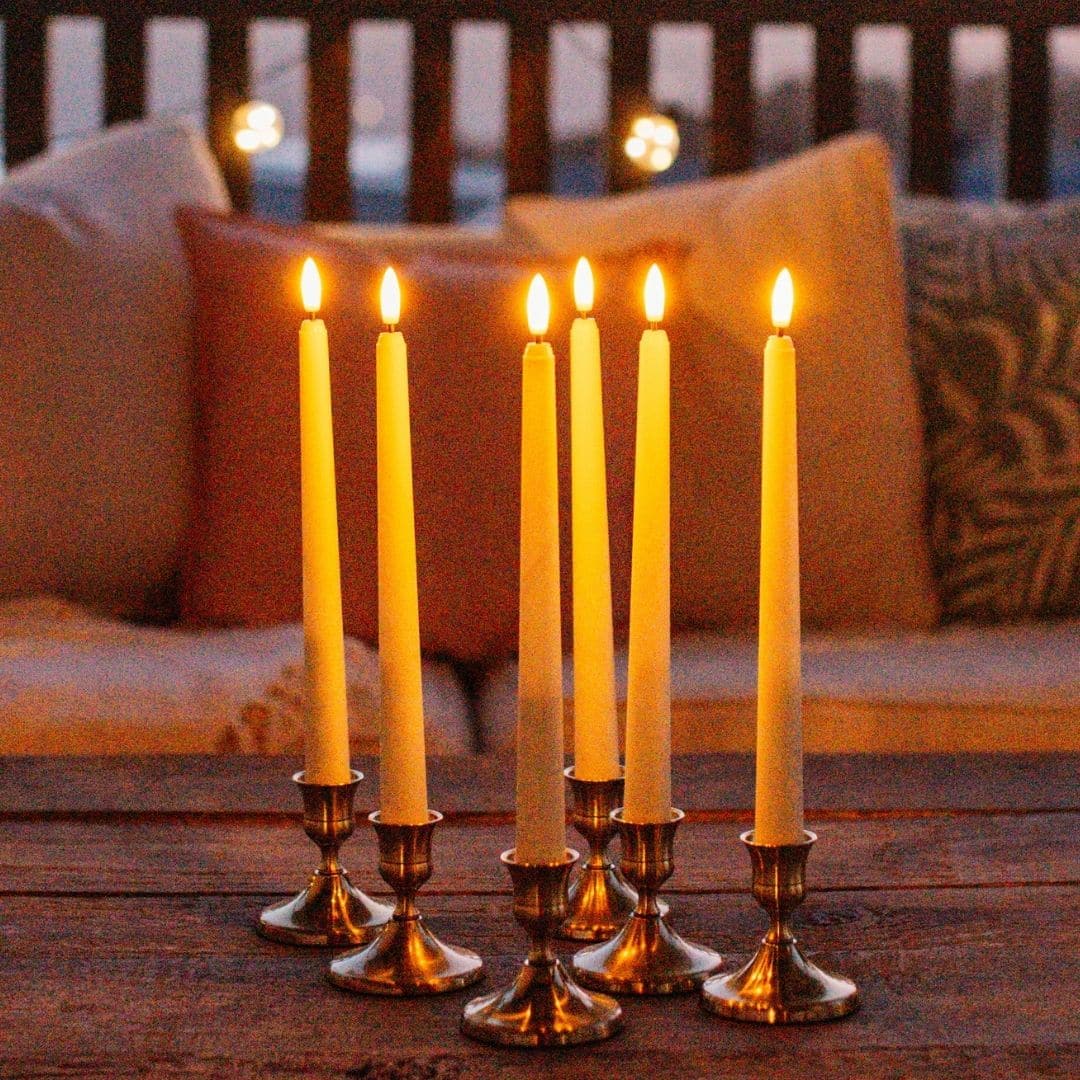 Ivory flameless LED taper candles in holders glowing softly on a dining table.