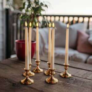 Ivory flameless LED taper candles in holders glowing softly on a dining table.