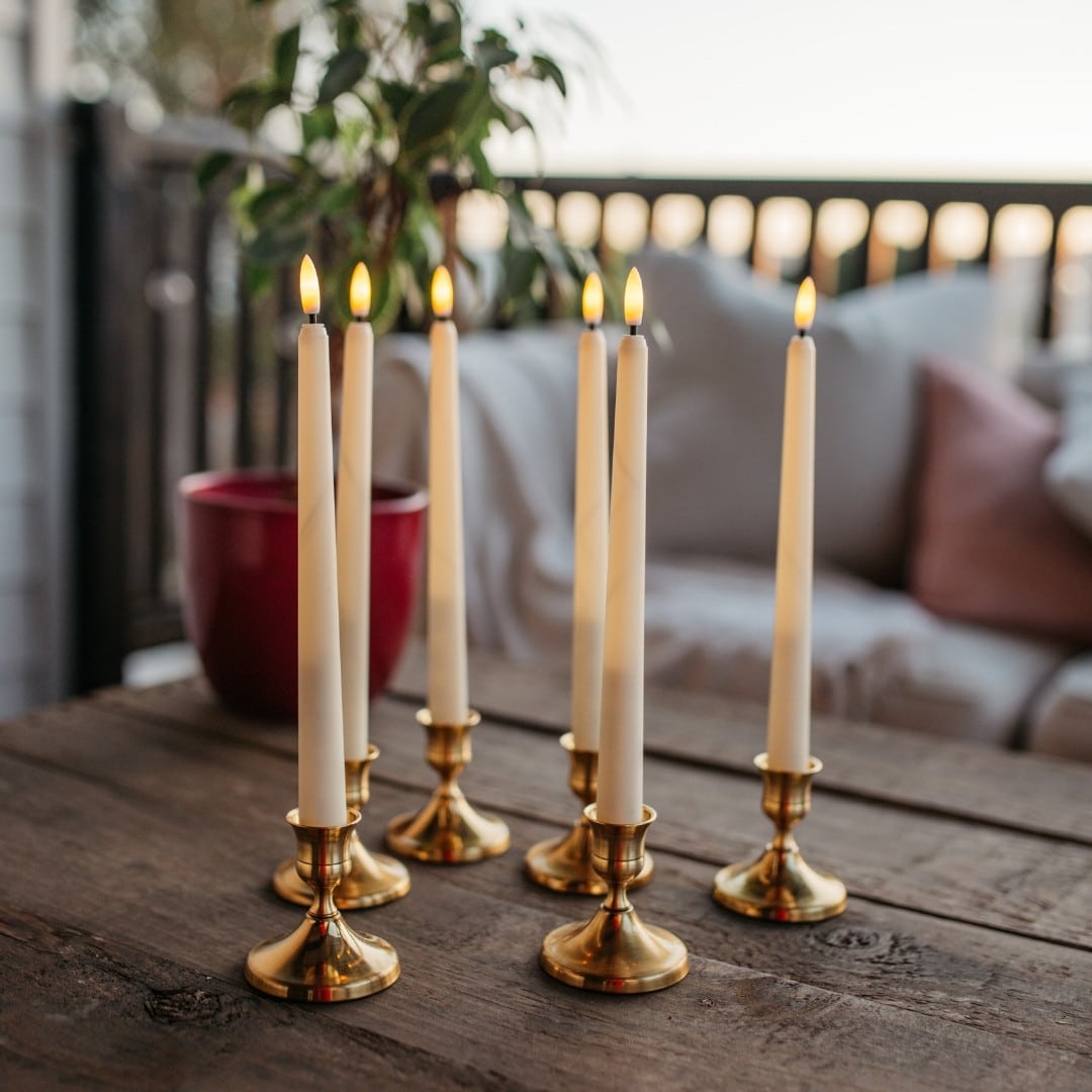 Ivory flameless LED taper candles in holders glowing softly on a dining table.