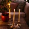 Ivory flameless LED taper candles in holders glowing softly on a dining table.