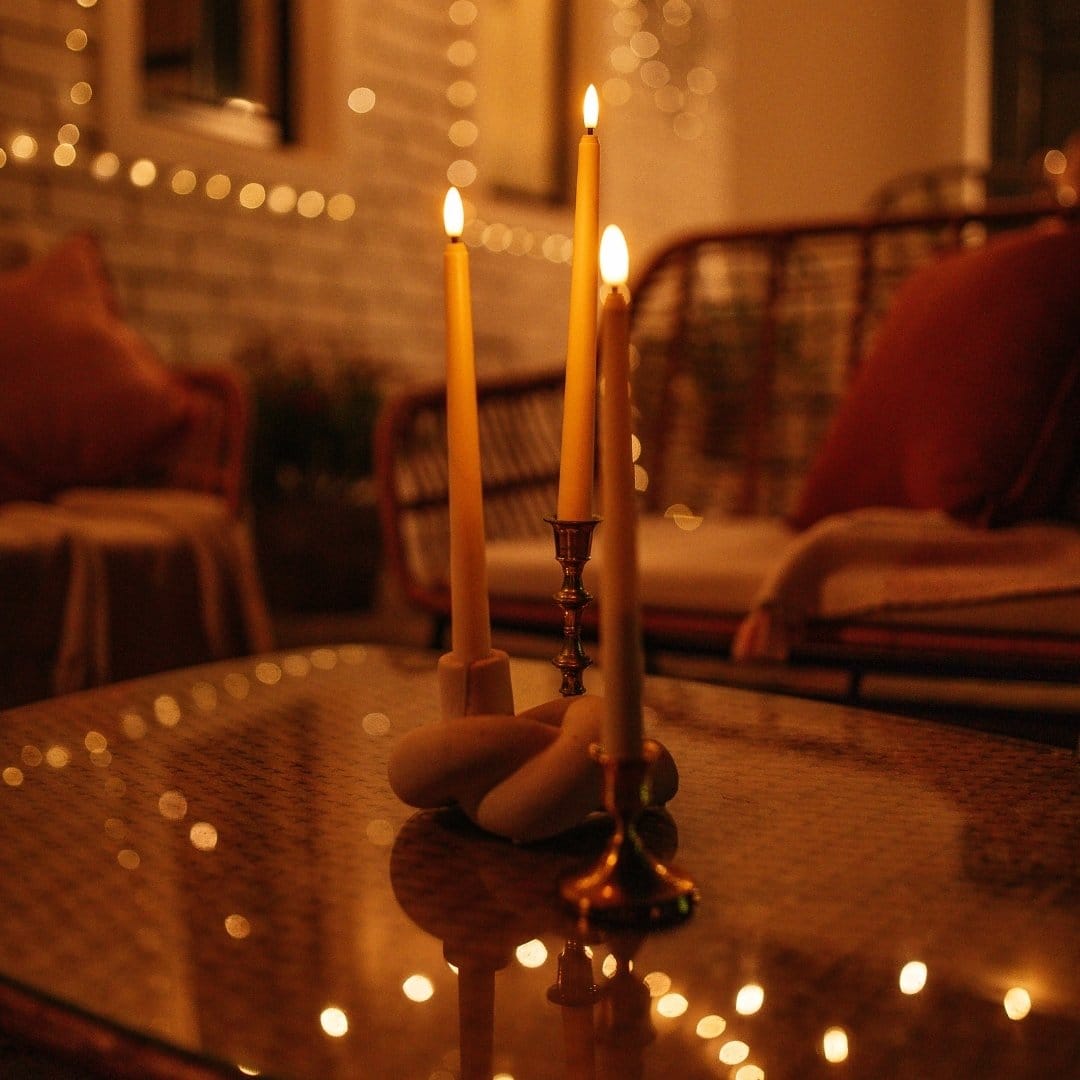 Ivory flameless LED taper candles in holders glowing softly on a dining table.