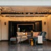 Classic String Lights Pro draped across a covered outdoor patio ceiling above a grey lounge set and coffee table with a lantern at dusk